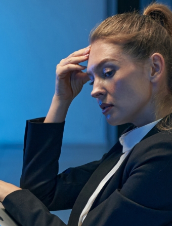 Woman in business suit holds her hand to her forehead and looks off to the side